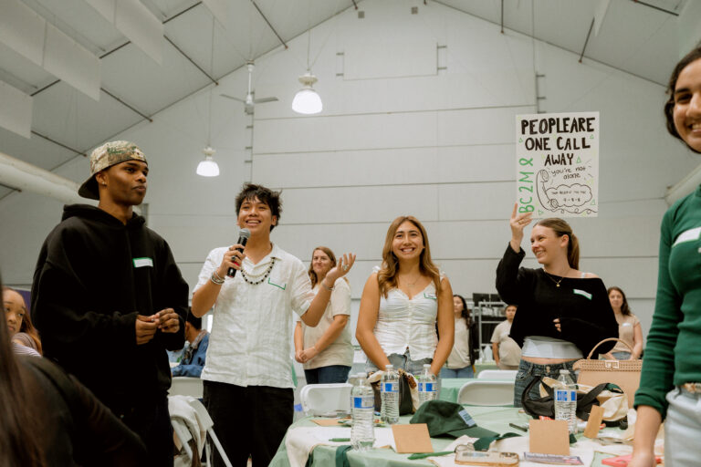 Students at a BC2M student summit, with one student speaking into a microphone and another holding a sign about support.