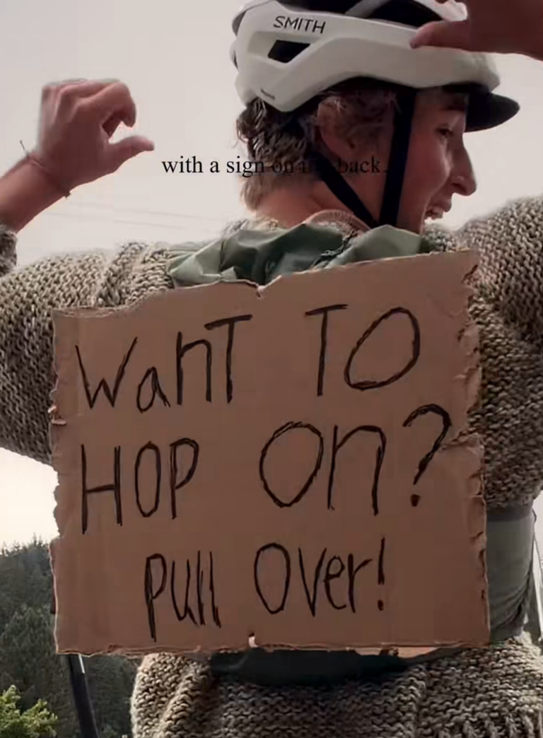 A cyclist on a tandem bike with a sign that says, "Want to hop on? Pull over!"